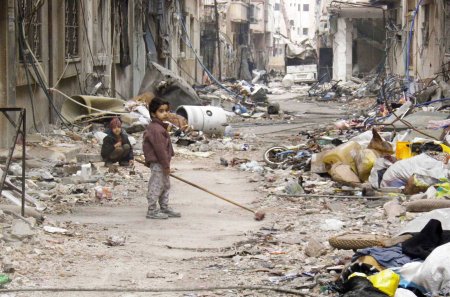 Image: A child clears damage and debris in the besieged area of Homs